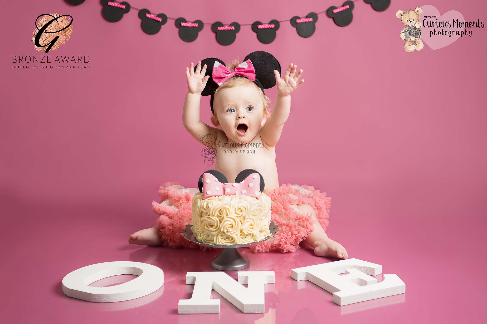 Award winning image of baby girls minnie mouse cake smash with baby hoding hands high in air with enjoyment
