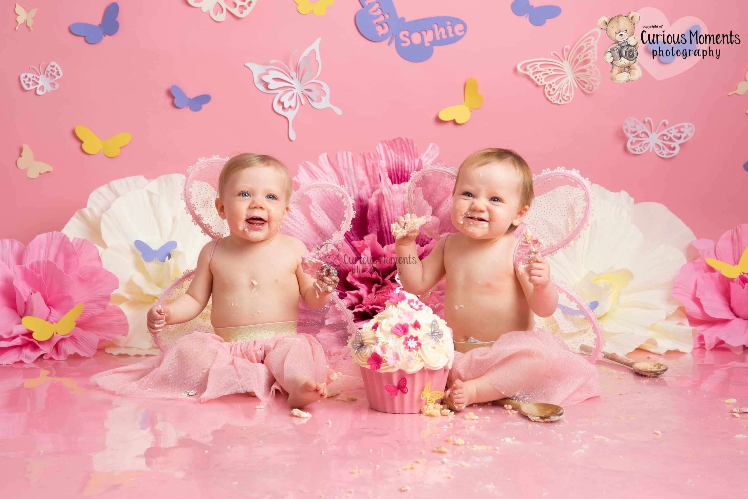 Twin girls cake smash on pink background with flowers and butterflies
