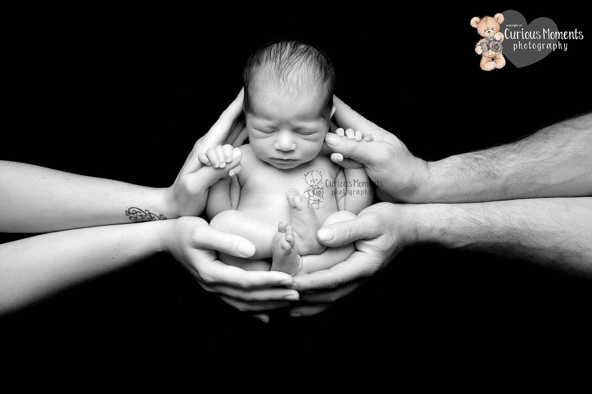 black and white image of baby nestled into the security of mum and dads hands