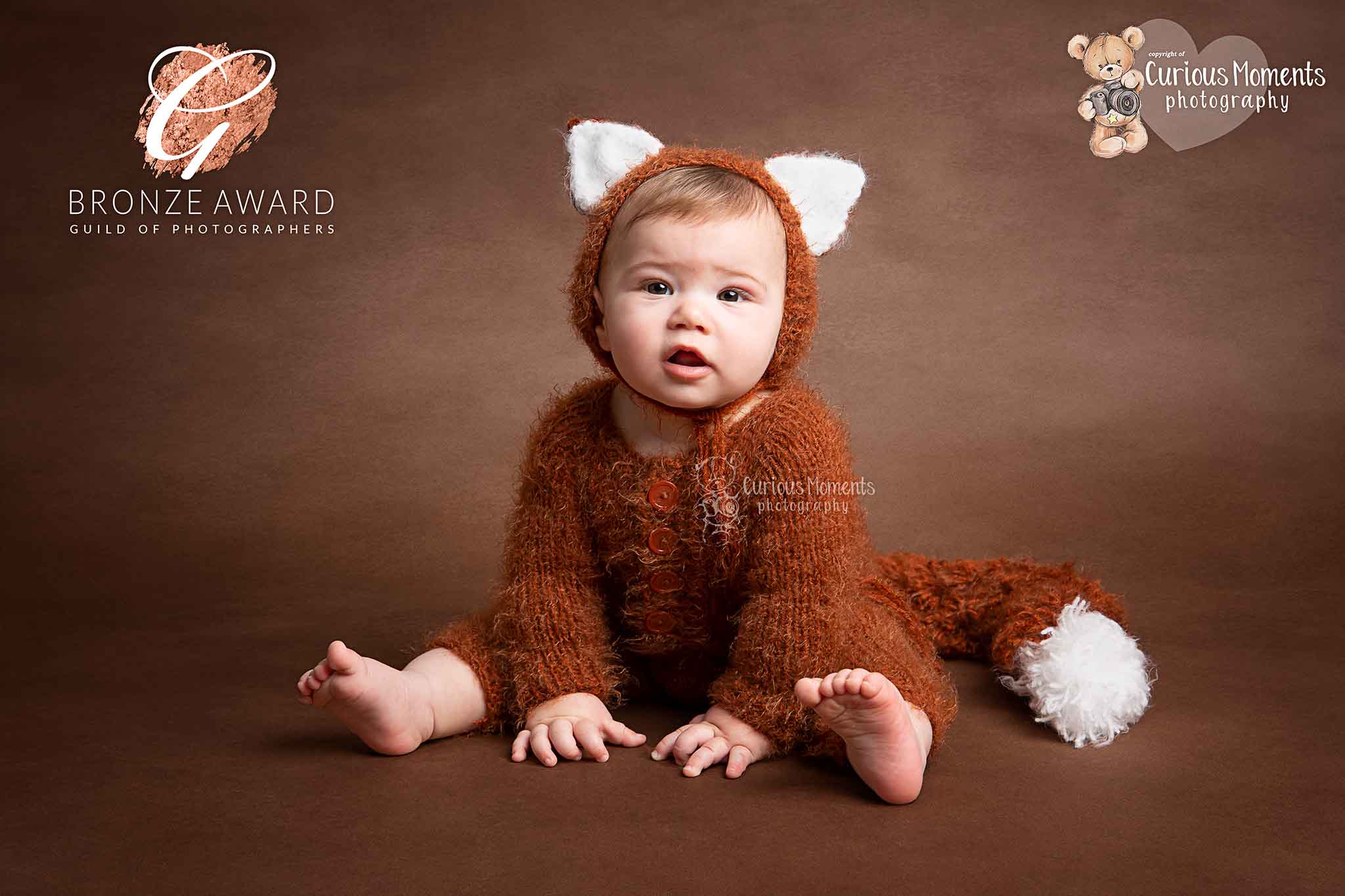 Award winning image taken by pembrokeshire photographer of baby boy wearing a knitted fox outfit sat on a brown backdrop