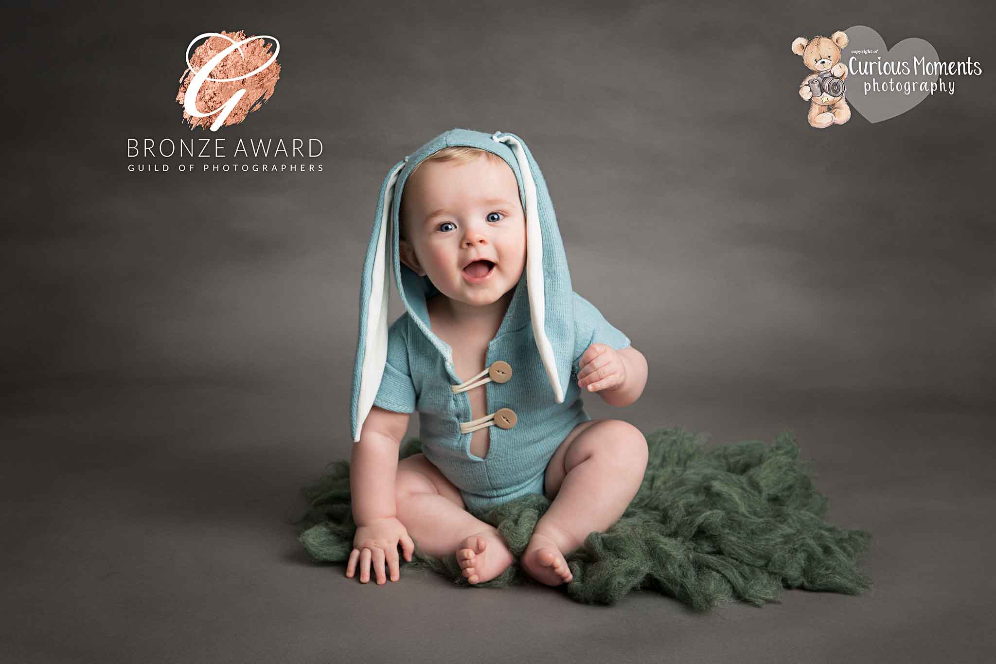 Award winning image of baby boy sat on grey background wearing a light green rabbit romper during photo shoot with carmarthenshire and Pembrokeshire photographer