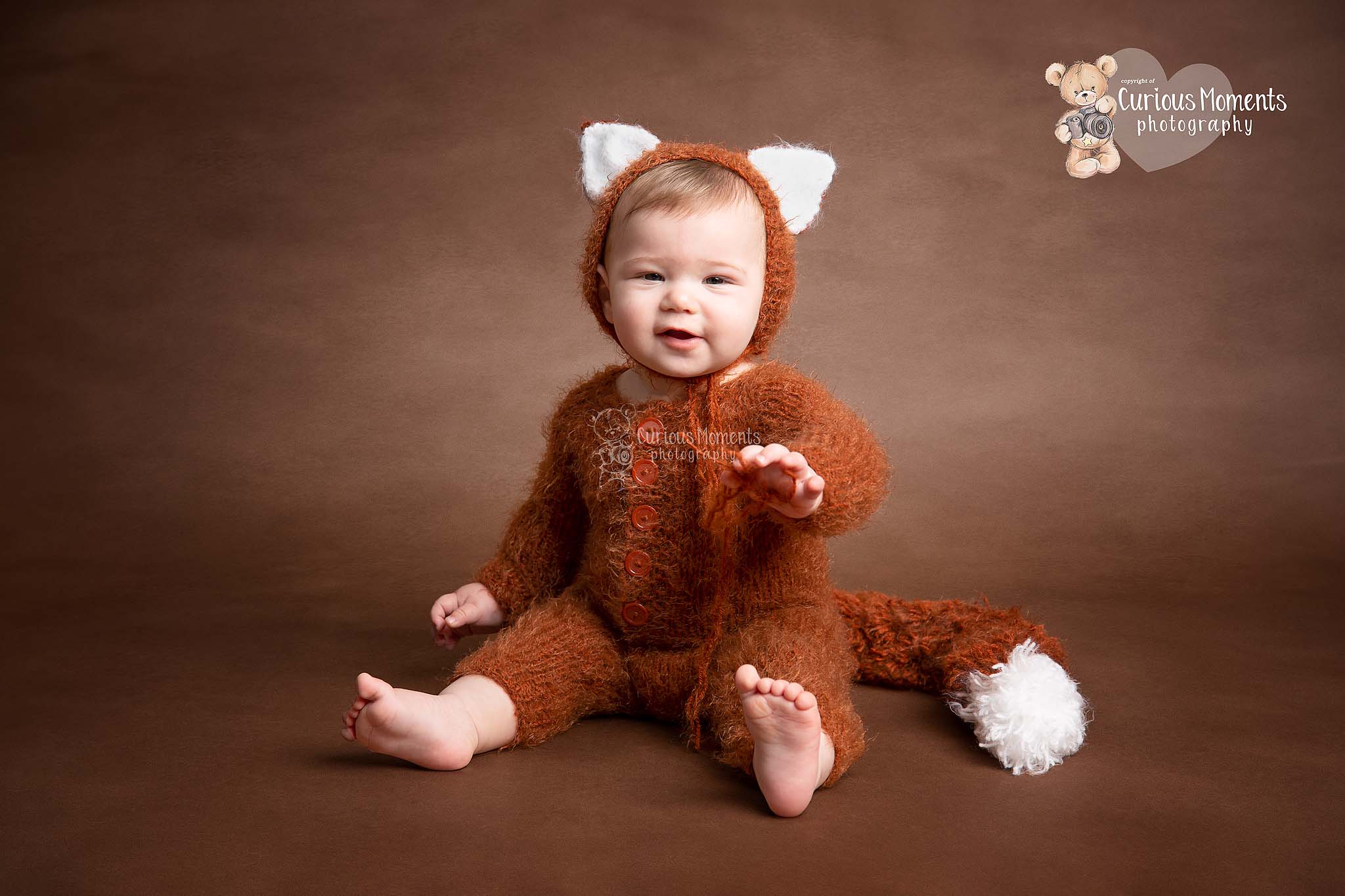 Baby Photographer Carmarthen photographs baby boy in fox outfit who is sitting and smiling at camera